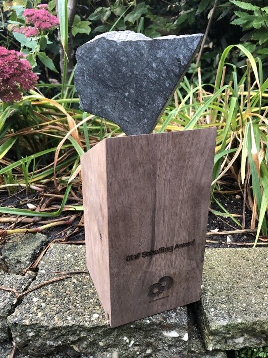 Olaf Schuiling Award, ontwerp Andy Dockett, uitvoering Fiction Factory Amsterdam. Een brok olivijn lijkt te zweven op een sokkel van hout.Afbeelding2